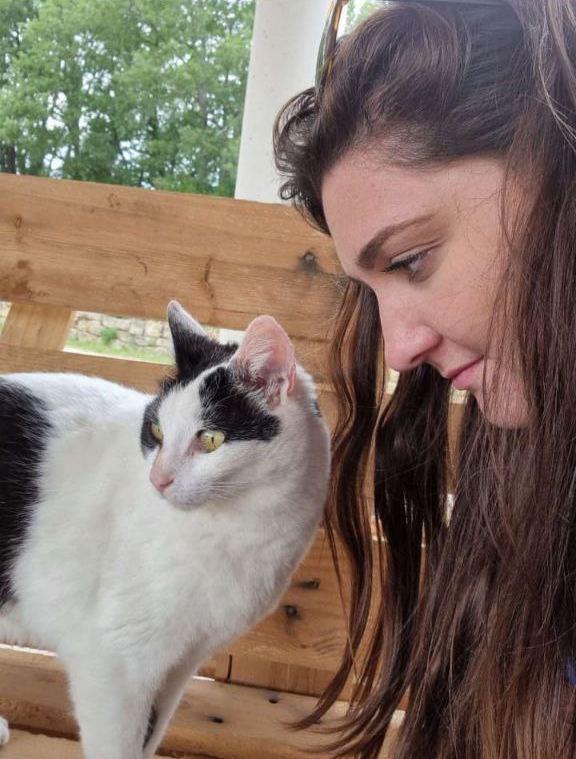 Photo avec la comportementaliste félin Émeline regardant avec son visage très rapprocher un chat blanc et noir sur un banc en bois